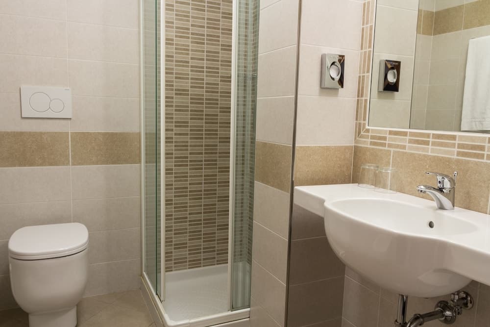 A modern bathroom with beige tiled walls, a glass-enclosed shower, a sleek white sink, and a toilet, ideal for travelers seeking clean and functional accommodations.