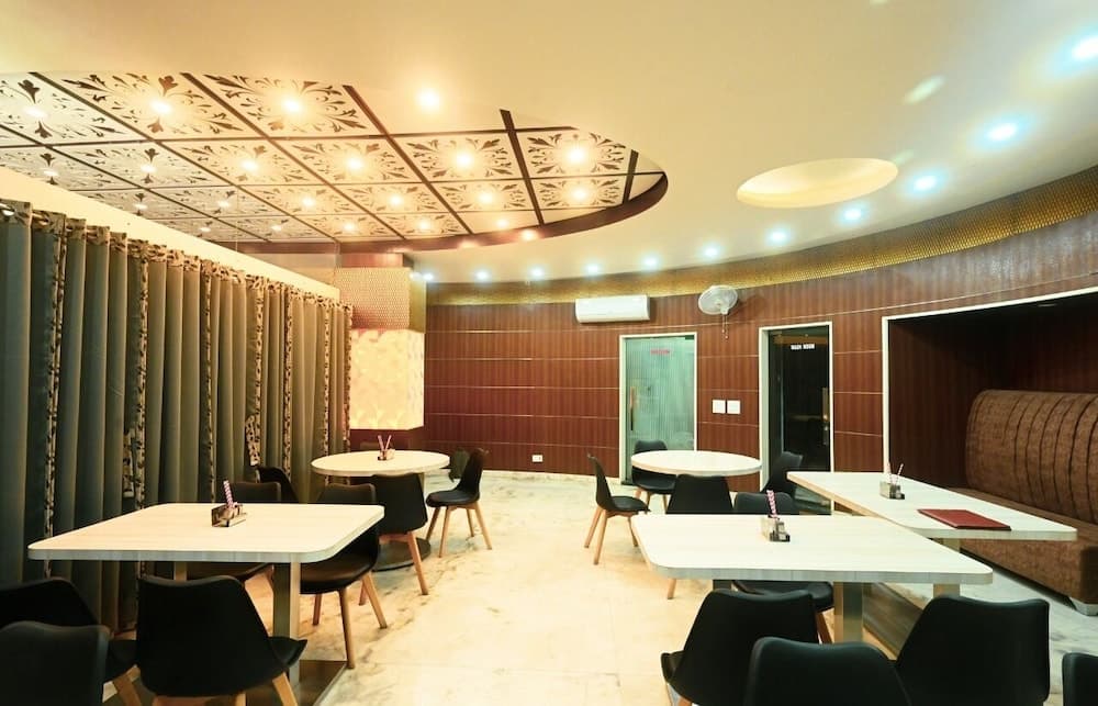 A cozy indoor dining area features elegant white tables, black chairs, decorative ceiling lights, and warm wooden walls, ideal for travelers seeking a comfortable and stylish restaurant experience.