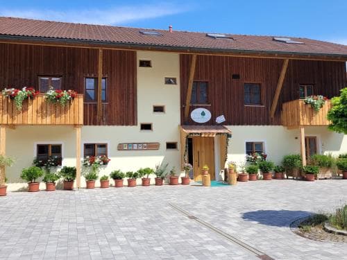 A charming rural lodge with wooden accents and flower-adorned balconies invites travelers to relax in its serene courtyard, perfect for a peaceful getaway.