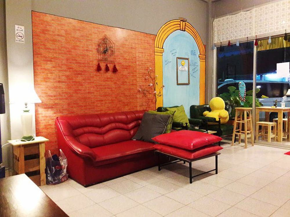 A cozy lounge area features a vibrant red leather sofa against a faux brick wall with artistic decorations, creating an inviting atmosphere ideal for travelers seeking relaxation in a hostel or café setting.