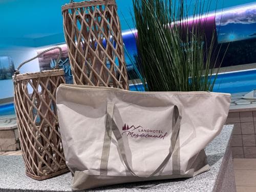 A cozy indoor setting features a branded tote bag from Landhotel Magdalenenhof resting beside wicker baskets and a potted plant, evoking a serene and inviting atmosphere ideal for travelers seeking relaxation and comfort.