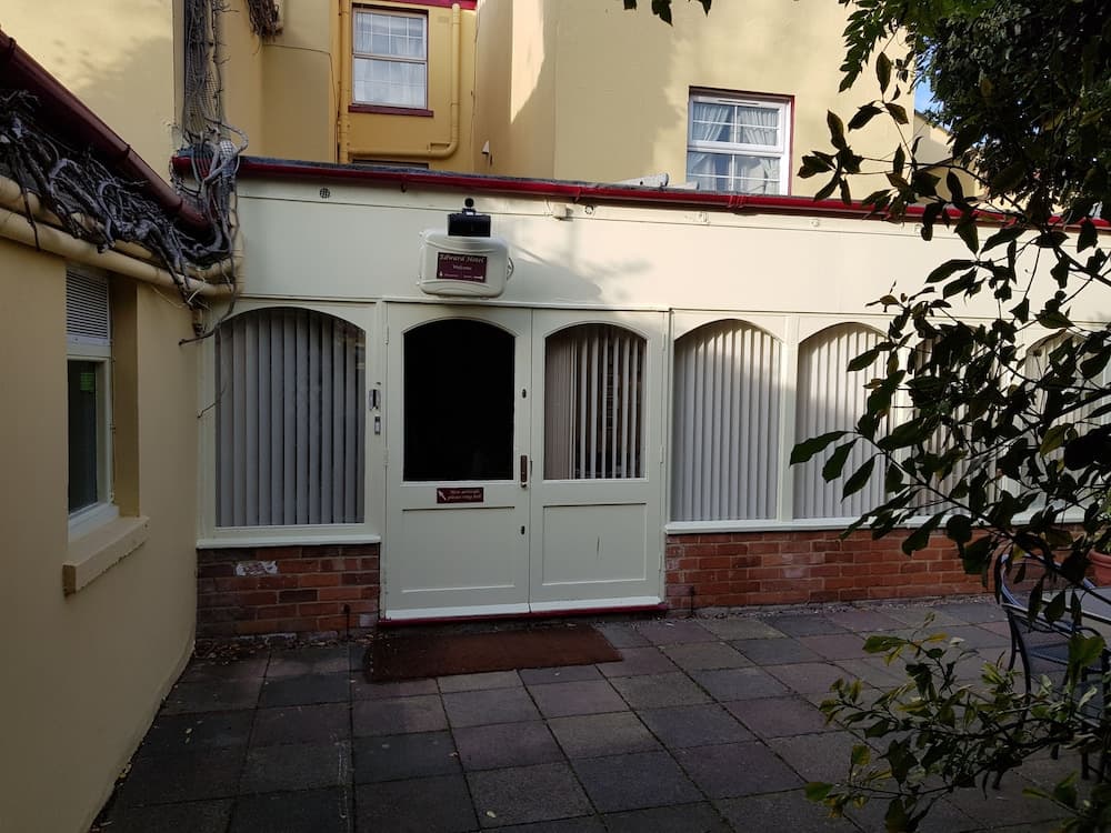 A serene courtyard entrance features a white double door flanked by arched windows, set against a yellow building with brick accents, ideal for travelers seeking quaint urban accommodations.