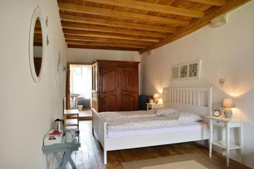 A cozy bedroom with rustic wooden beams, a white bed, and warm lighting creates an inviting atmosphere in a charming countryside retreat, perfect for travelers seeking relaxation and comfort.