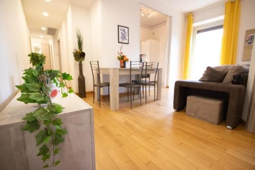 A cozy apartment interior featuring hardwood floors, modern furniture, vibrant yellow curtains, and lush green plants, ideal for travelers seeking a comfortable and stylish short-term rental experience.