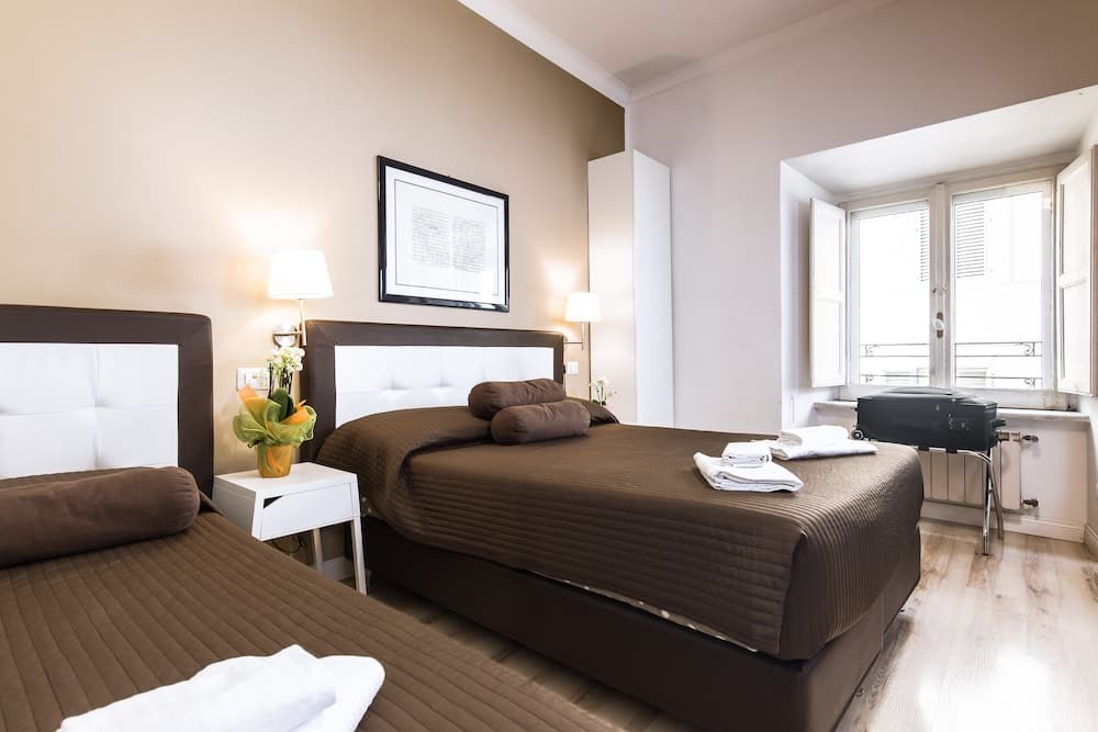 A cozy hotel room with two neatly made beds, soft lighting, and a window view of a balcony offers a comfortable stay for travelers seeking relaxation.