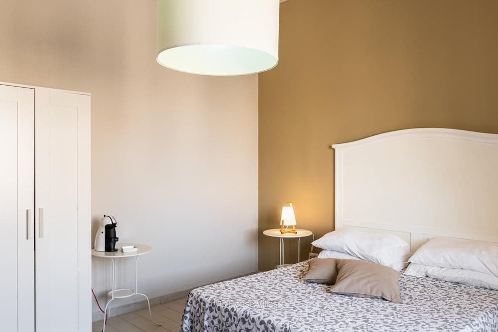 A cozy bedroom with warm-toned walls, a neatly made bed adorned with patterned linens, a softly glowing bedside lamp, and a minimalist coffee setup on a small table, ideal for travelers seeking a serene and stylish retreat.
