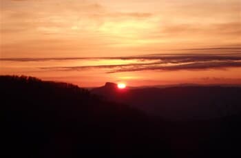 A breathtaking sunset casts warm hues over a serene mountain vista, ideal for tranquil hiking adventures and capturing nature's beauty in photography.