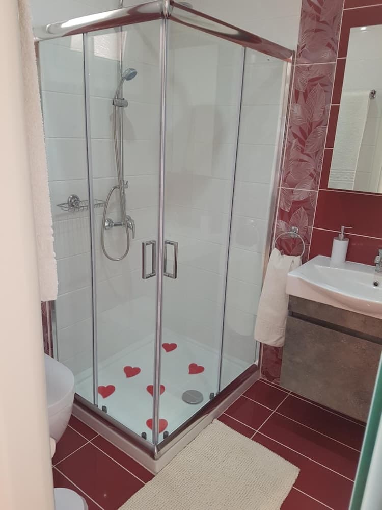 A cozy bathroom with red heart-shaped decorations in the shower, featuring modern fixtures, a sink with a mirror, and a warm ambiance ideal for romantic getaways or intimate stays.