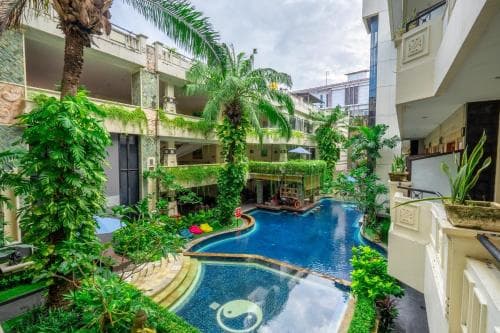 A serene tropical courtyard features lush greenery surrounding a vibrant blue pool, ideal for relaxing stays in a resort-like setting.