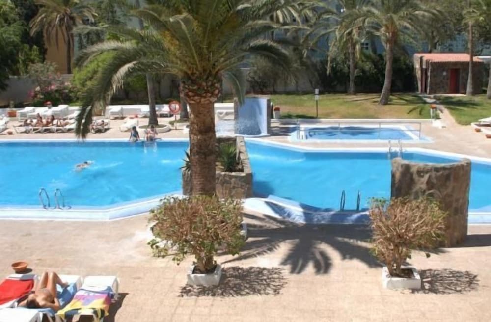 A serene resort scene features vibrant blue pools surrounded by palm trees and lounging guests, ideal for a relaxing vacation getaway.