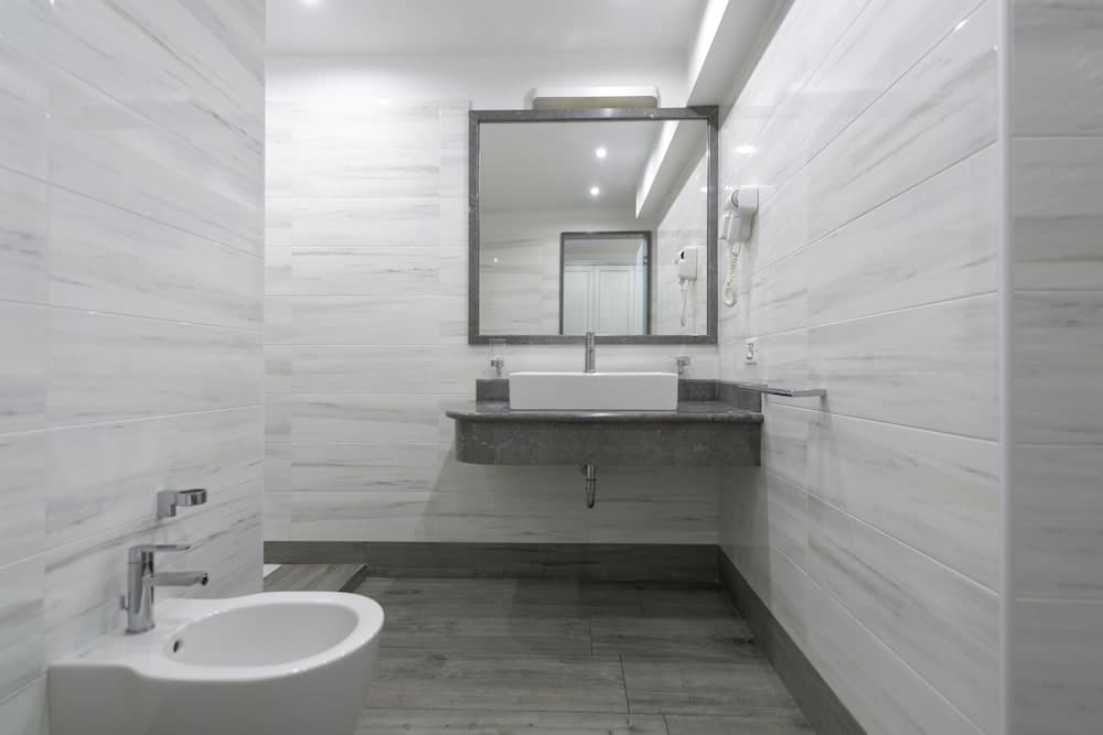 A modern bathroom with sleek marble walls, a floating sink vanity, and a bidet, exudes a clean and luxurious ambiance ideal for showcasing hotel amenities in travel listings.