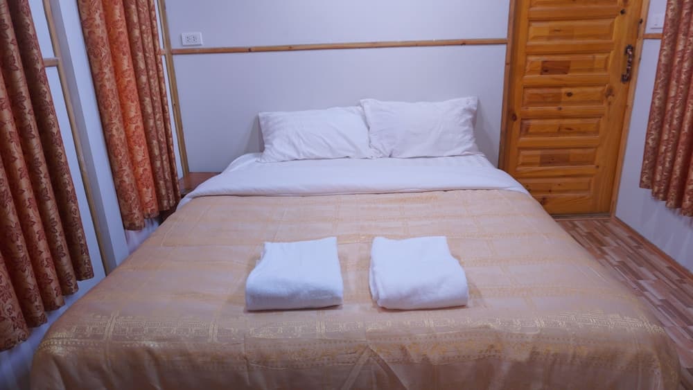 A cozy hotel room features a neatly made bed with white towels, patterned curtains, and wooden furnishings, ideal for travelers seeking comfort and simplicity.