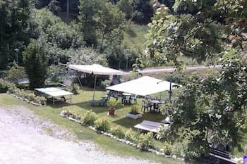 A serene riverside picnic area with shaded tables under umbrellas, surrounded by lush greenery, offers a tranquil spot for outdoor gatherings and relaxation.