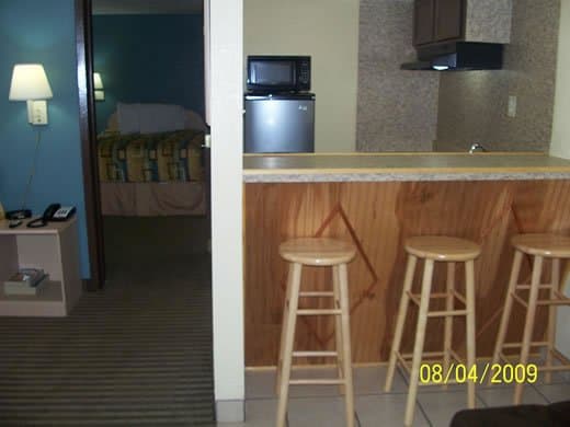 A cozy motel room with a kitchenette featuring wooden bar stools, a microwave, and a refrigerator, exudes a warm and inviting atmosphere ideal for travelers seeking comfort and convenience.