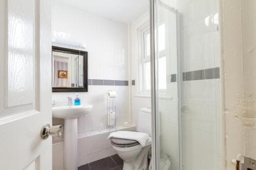 A bright, clean bathroom with white fixtures, a glass shower enclosure, and a small window creates a serene atmosphere, ideal for travelers seeking a cozy and functional accommodation space.