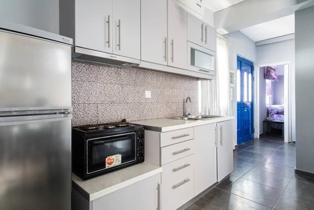 A cozy apartment kitchen with white cabinetry, stainless steel appliances, and a blue door leading to a bedroom, ideal for travelers seeking self-catering accommodations.