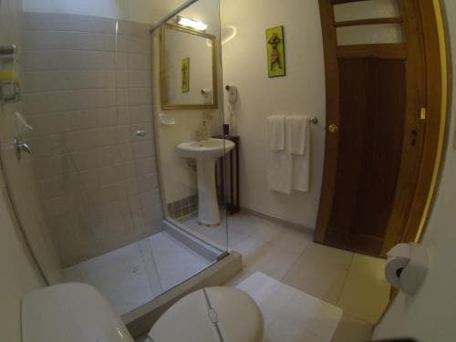 A cozy hotel bathroom features a glass-enclosed shower, pedestal sink, neatly folded towels, and warm wooden accents, ideal for travelers seeking comfort and cleanliness.