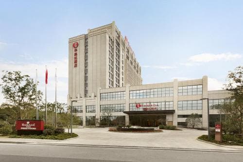 A modern hotel complex with a prominent glass facade and a clear sky backdrop offers a welcoming atmosphere for travelers seeking comfortable accommodations in an urban setting.