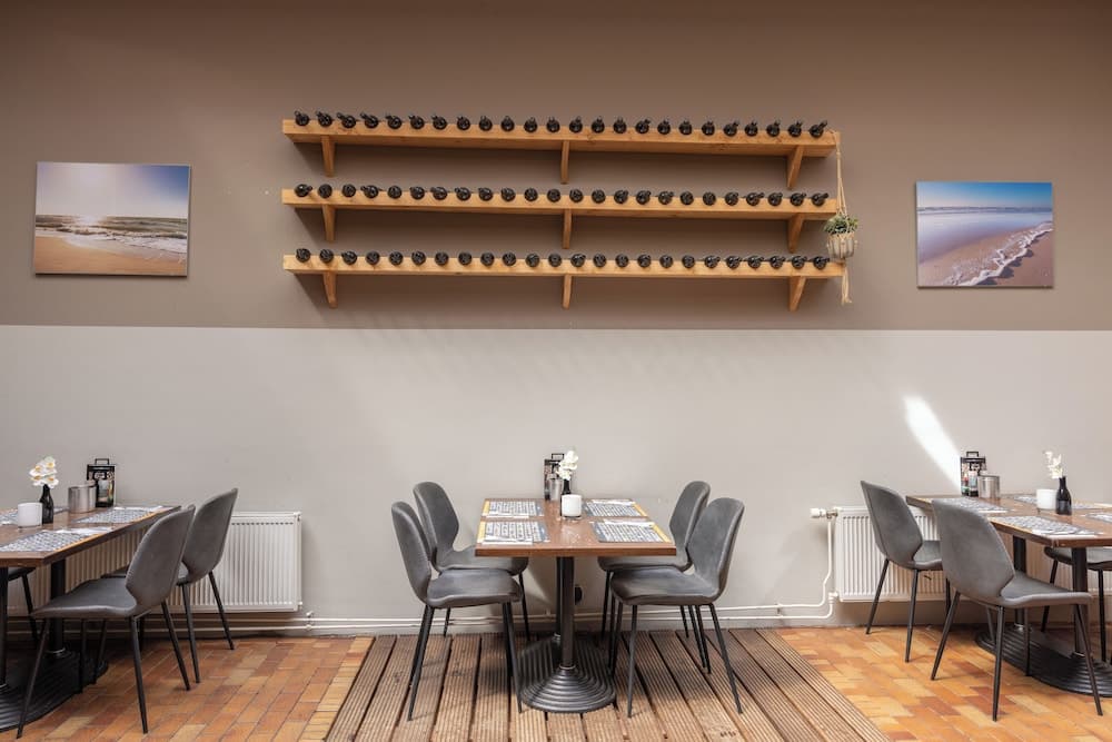A cozy café with wooden tables, gray chairs, and shelves lined with small black birds creates an inviting atmosphere, perfect for travelers seeking a quiet spot to relax and enjoy a meal.