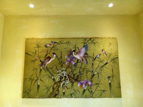 A vibrant mural of birds and flowers adorns a yellow wall in an indoor space, creating a serene and artistic atmosphere ideal for cultural exploration or relaxation.