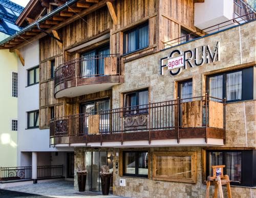 A cozy alpine apartment building with rustic wooden balconies and modern signage invites travelers seeking a charming mountain retreat.