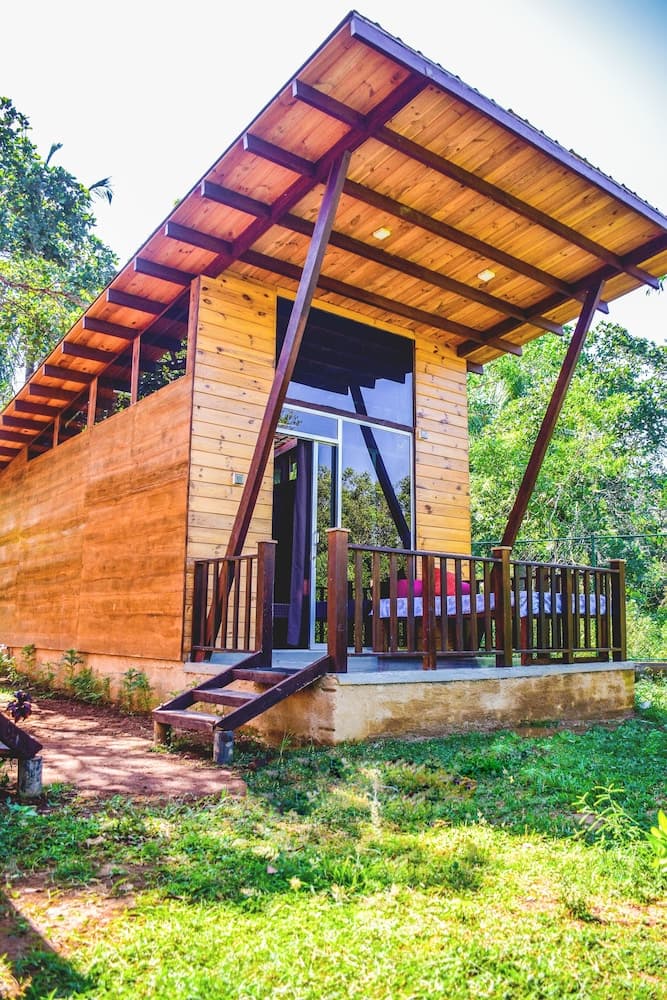 A serene wooden cabin with a spacious porch and glass doors stands amidst lush greenery, ideal for eco-friendly retreats and nature lovers seeking tranquility.