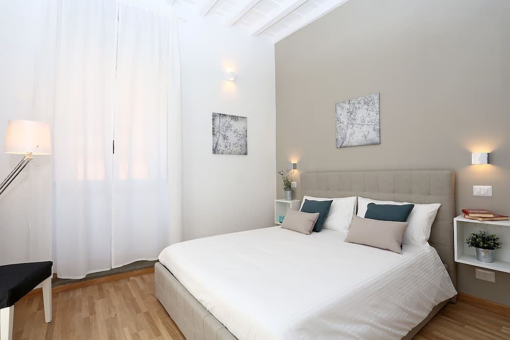A cozy bedroom with a neatly made bed, soft lighting, wooden floors, and minimalist decor offers a serene retreat for travelers seeking relaxation.