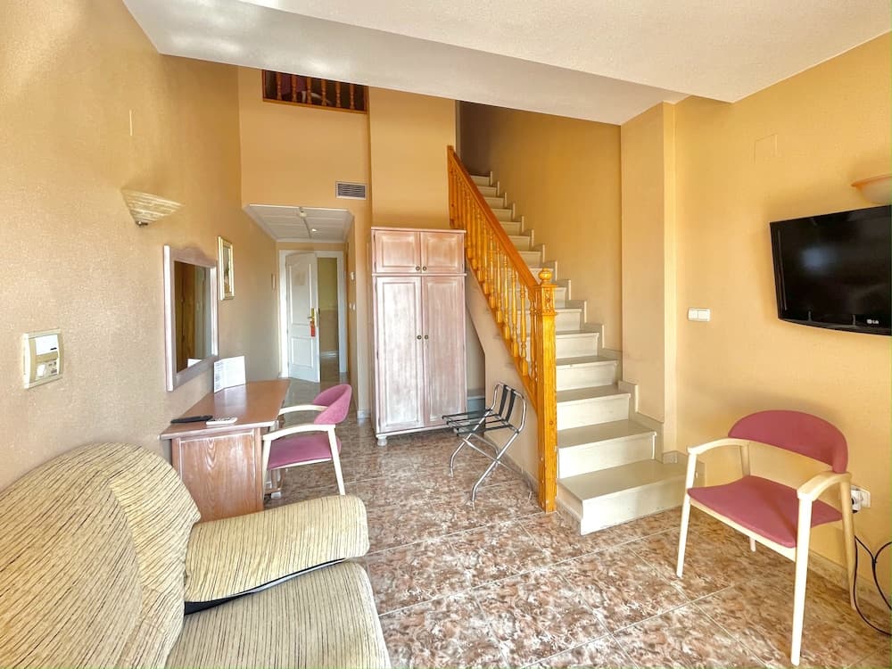 A cozy apartment interior features warm yellow walls, a staircase with wooden railings, comfortable seating, and a desk area, ideal for travelers seeking a homey and functional stay.