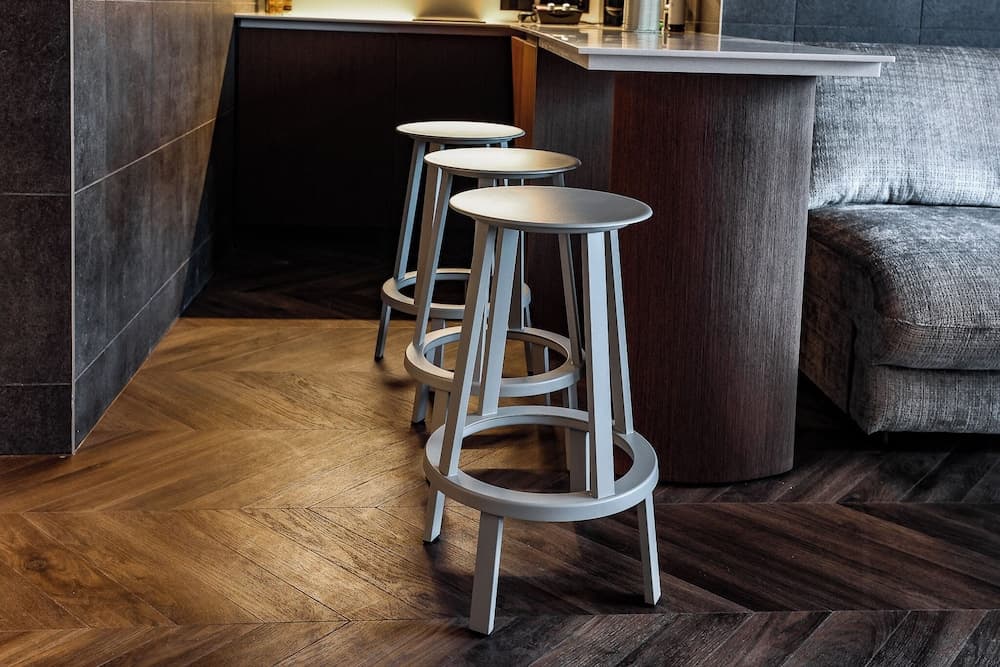 A cozy modern kitchen corner features sleek bar stools on a herringbone-patterned wooden floor, ideal for travelers seeking stylish urban accommodations.