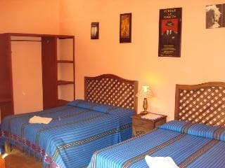 A cozy budget-friendly hotel room features two neatly made beds with blue patterned bedding, warm orange walls adorned with framed posters, and simple wooden furniture, ideal for travelers seeking comfort on a budget.