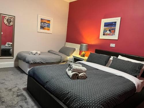 A cozy hotel room features two neatly made beds with patterned bedding, a vibrant red accent wall, framed artwork, and soft lighting, ideal for travelers seeking comfort and relaxation.