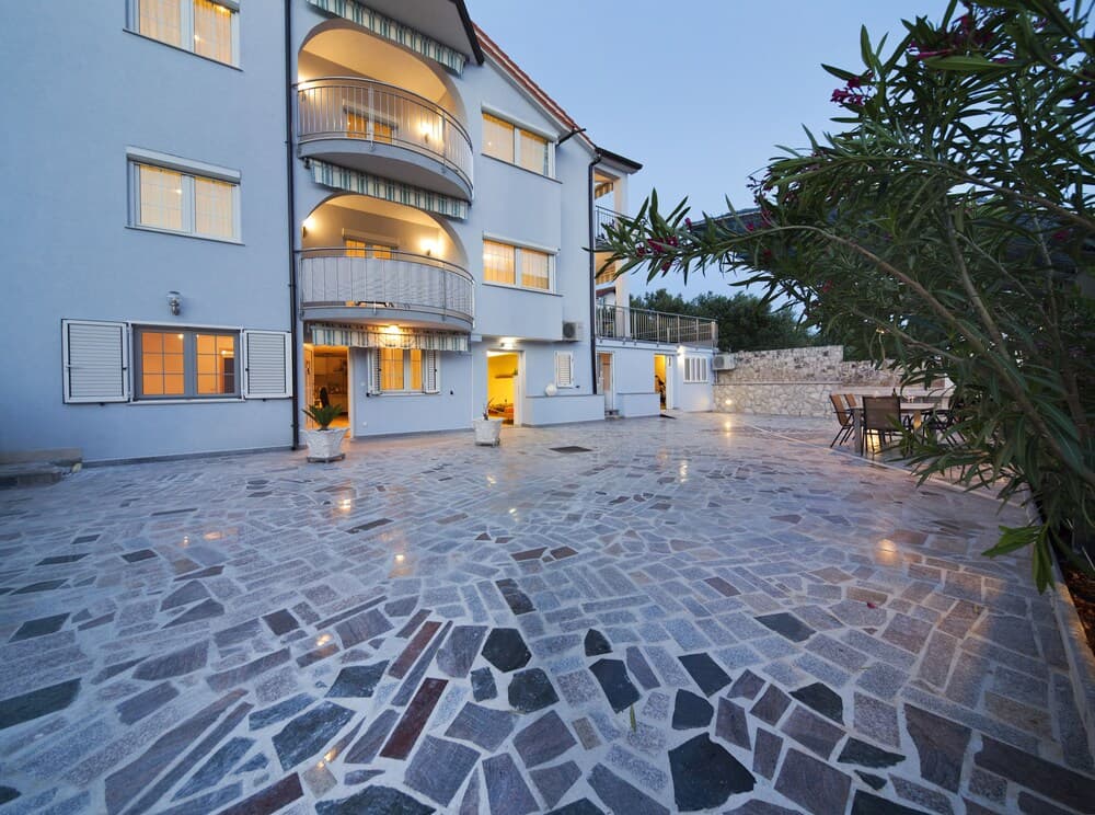 A serene evening at a charming villa courtyard with stone-paved flooring, illuminated balconies, and lush greenery, ideal for travelers seeking a cozy and picturesque retreat.