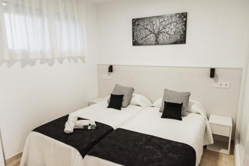 A cozy hotel room features a neatly made bed adorned with black and white linens, a minimalist wall art piece, and soft lighting, creating a serene atmosphere ideal for travelers seeking relaxation.