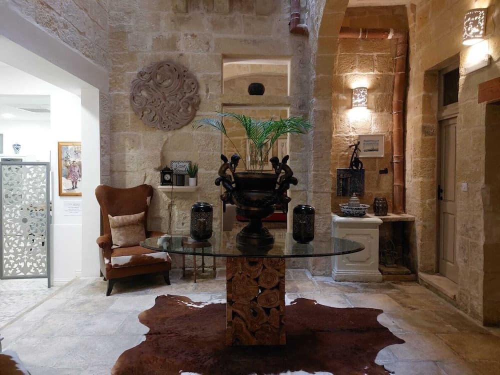 A cozy indoor lounge area features rustic stone walls, warm lighting, and eclectic decor including a cowhide rug, ornate table centerpiece, and leather armchair, ideal for travelers seeking a charming and inviting retreat.