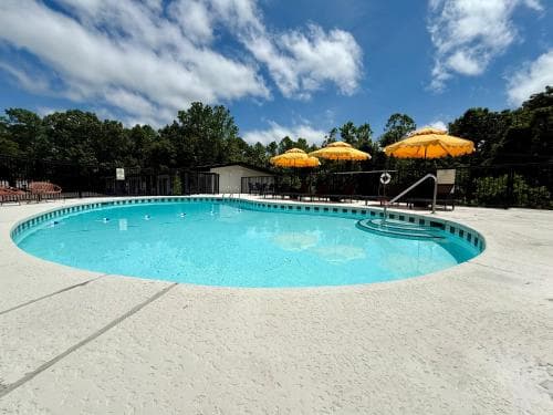 A serene outdoor swimming pool surrounded by lush greenery under a partly cloudy sky, featuring vibrant yellow umbrellas and lounge chairs, ideal for a relaxing vacation getaway.