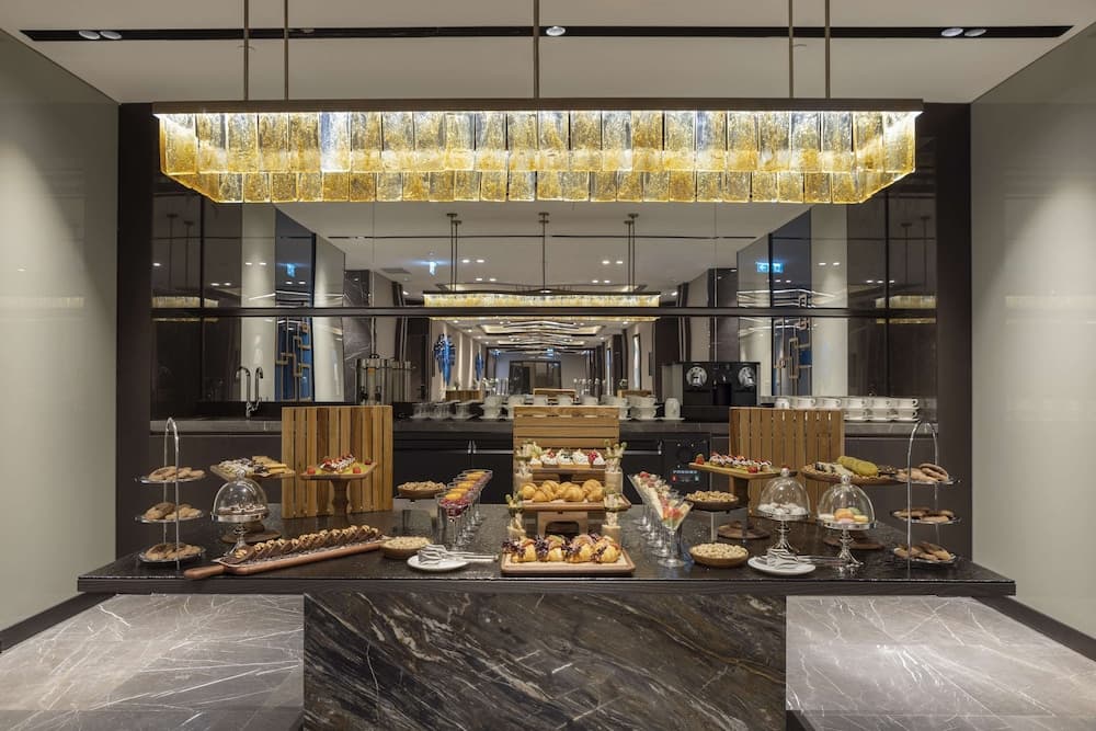 A luxurious hotel buffet area features an elegant marble counter adorned with assorted pastries and desserts under a shimmering glass chandelier, creating a sophisticated ambiance ideal for travelers seeking a premium dining experience.