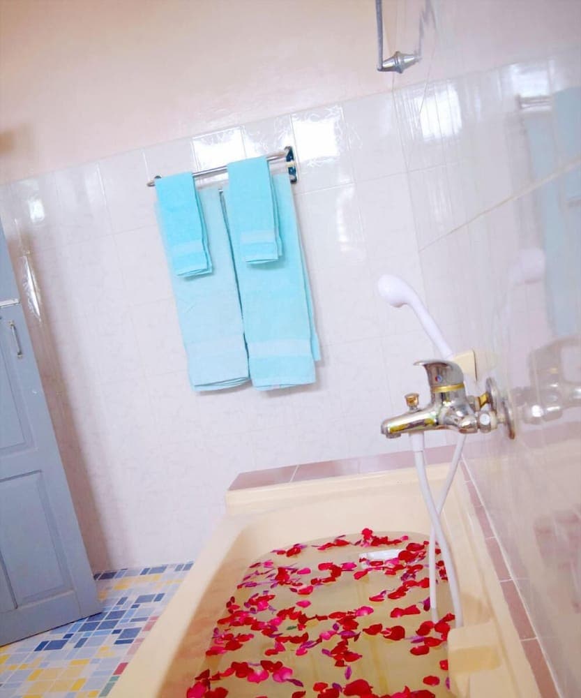 A serene bathroom scene features a bathtub filled with water and floating red rose petals, complemented by neatly hung blue towels on a rack, ideal for travelers seeking relaxation and comfort in their accommodations.