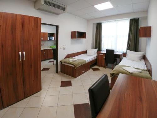 A cozy studio apartment features two single beds, a kitchenette, and wooden furnishings, ideal for budget-friendly travelers seeking comfort in a compact space.