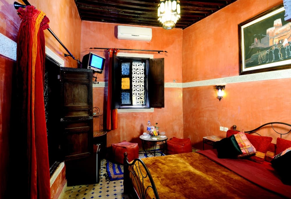 A cozy, warmly-lit Moroccan-style bedroom with vibrant orange walls, patterned textiles, and traditional decor invites travelers seeking a cultural and intimate stay experience.