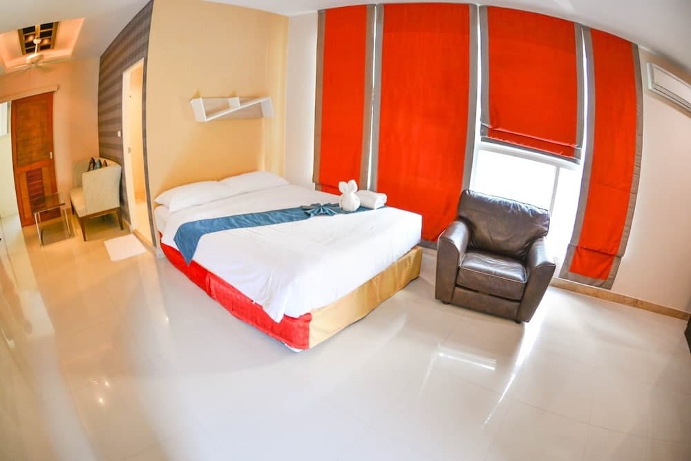 A cozy hotel room features a neatly made bed adorned with a towel animal, vibrant orange curtains, a leather armchair, and glossy tiled floors, ideal for travelers seeking comfort and style.