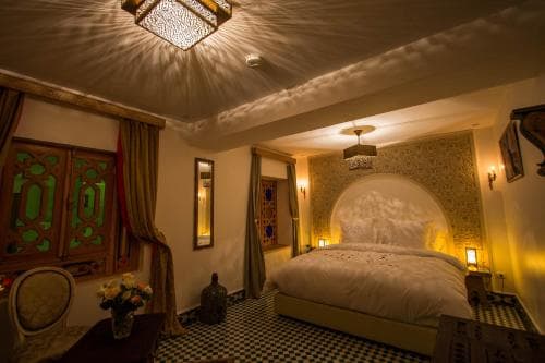 A cozy, warmly lit bedroom with intricate Moroccan-style decor, featuring patterned tiles, ornate wooden doors, and soft lighting, creates an inviting atmosphere ideal for a luxurious retreat experience.