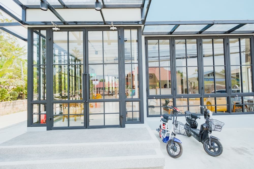 A modern glass-fronted building with scooters parked outside exudes a serene and inviting atmosphere, perfect for travelers seeking a stylish café or boutique in a tranquil urban setting.