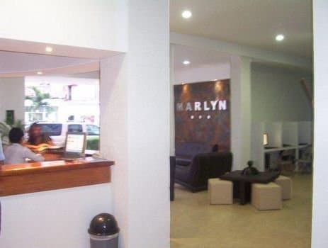 A cozy hotel lobby with a reception desk, lounge seating, and a "MARLYN" sign creates a welcoming atmosphere ideal for travelers seeking relaxation and convenience.