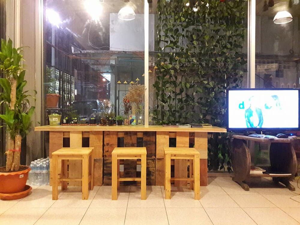 A cozy indoor café space features rustic wooden tables and stools surrounded by lush greenery and ambient lighting, ideal for travelers seeking a relaxing spot to unwind and enjoy a quiet moment.