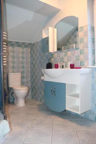 A cozy bathroom with blue-tiled walls, a modern vanity, and a mirrored cabinet offers a serene space for travelers seeking comfort in their accommodations.