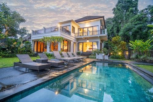 A serene tropical villa at dusk features a tranquil poolside area with lounge chairs, surrounded by lush greenery, ideal for a relaxing vacation retreat.