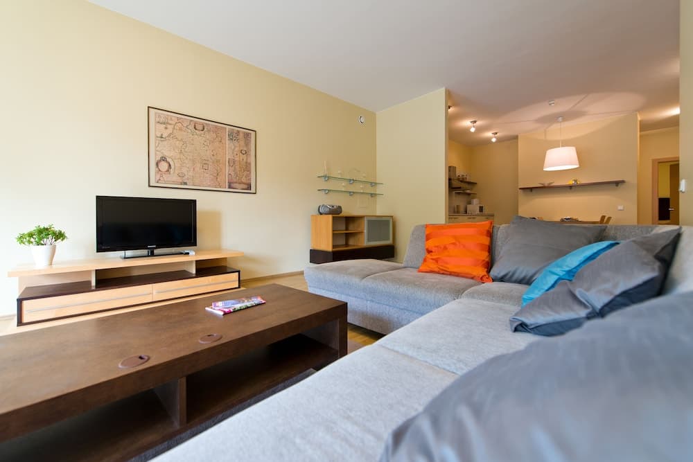 A cozy living room with modern furnishings, including a gray sofa adorned with colorful pillows, a wooden coffee table, and a flat-screen TV, creates an inviting atmosphere ideal for travelers seeking comfortable accommodation.