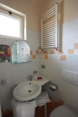 A cozy hotel bathroom features a white sink, tiled walls with orange accents, a towel warmer, and natural light from a window, ideal for travelers seeking comfort and functionality.