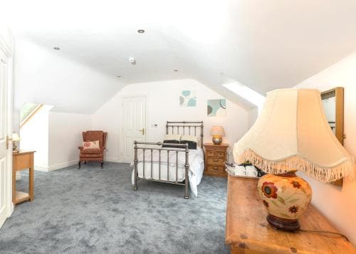 A cozy attic bedroom with soft lighting, a metal bedframe, wooden furniture, and a floral lamp creates a serene retreat ideal for travelers seeking a peaceful stay.