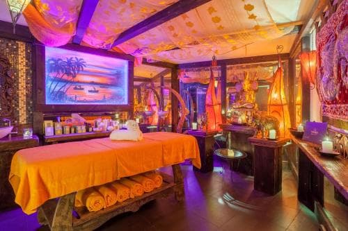 A vibrant spa room adorned with colorful fabrics, glowing lights, and tropical decor creates a serene atmosphere ideal for relaxation and wellness retreats.